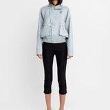 A model stands against a plain white studio background wearing a light blue cropped jacket, black cropped pants, and black-and-white striped high-heeled sandals.