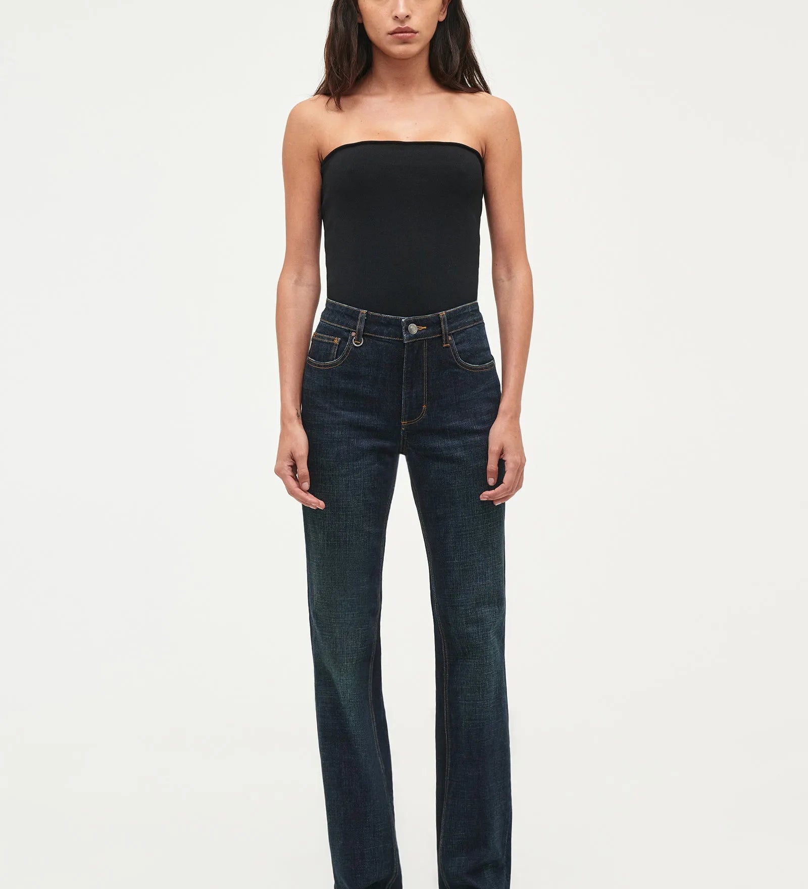 Woman wearing a black strapless top and dark blue jeans on a white background
