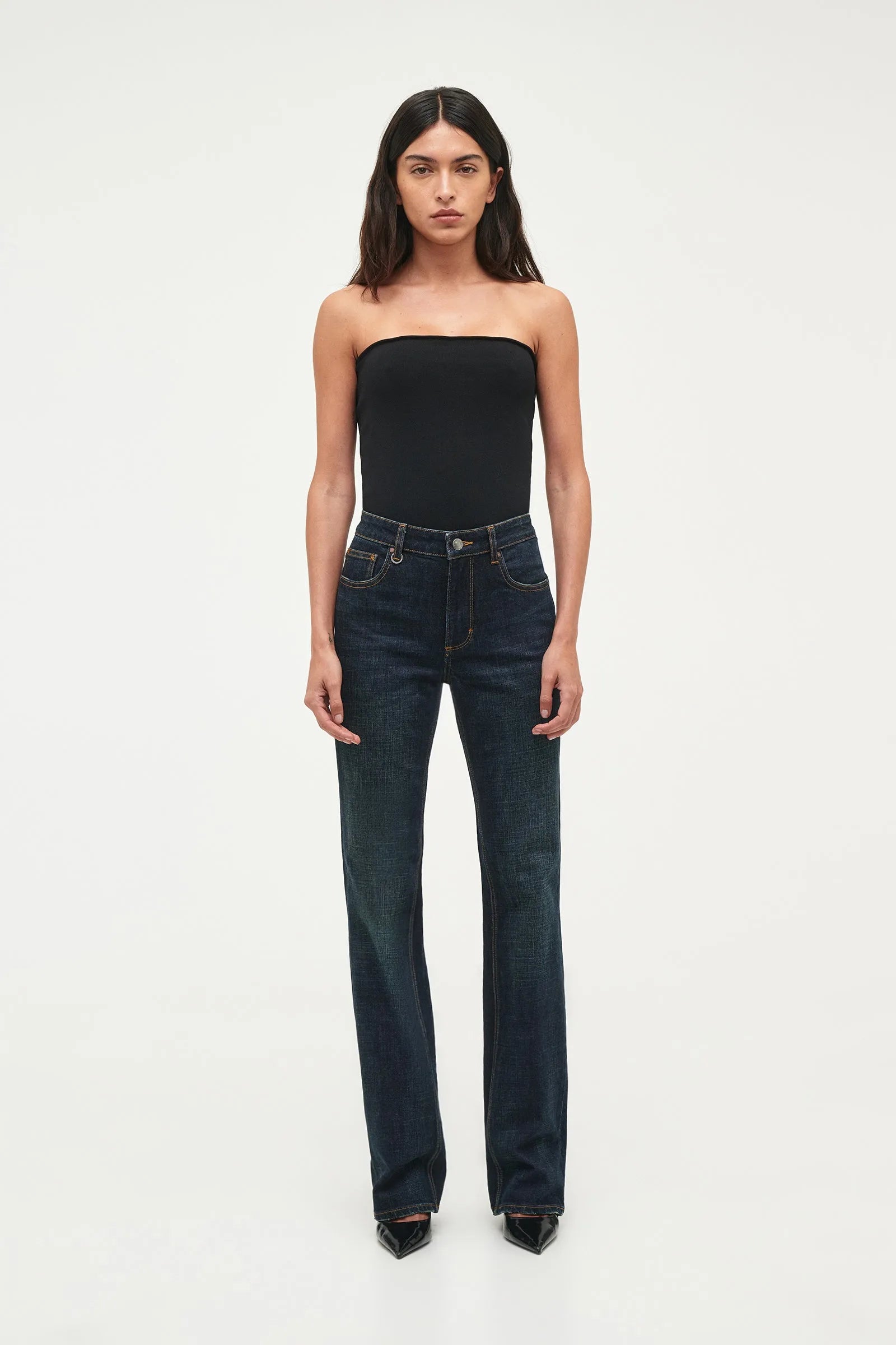 Woman wearing a black strapless top and dark blue jeans on a white background
