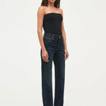 A model wearing dark wash, straight-leg jeans and a black strapless top, standing against a plain white studio background.