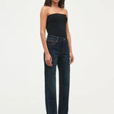 A model wearing dark wash, straight-leg jeans and a black strapless top, standing against a plain white studio background.