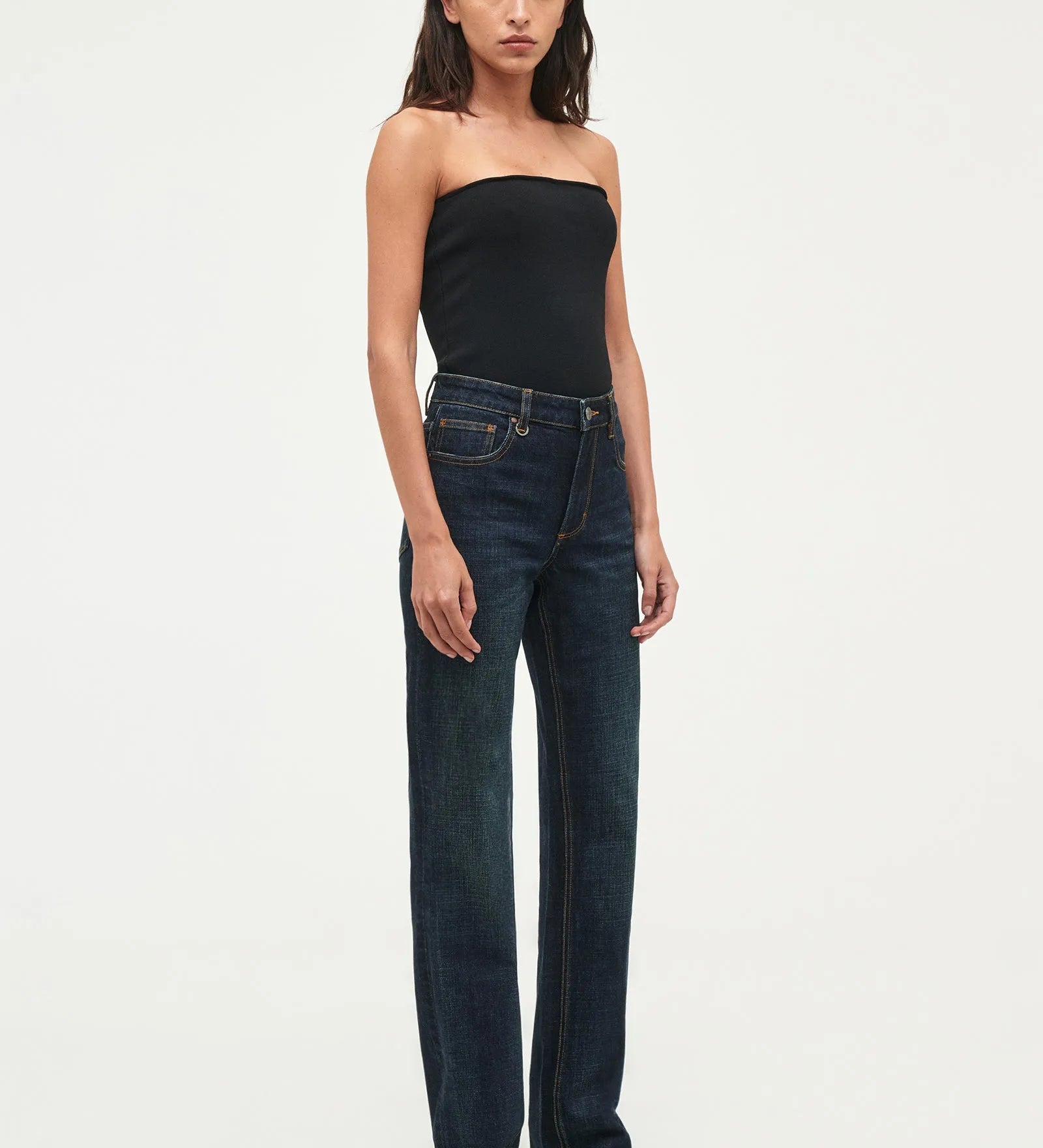 A model wearing dark wash, straight-leg jeans and a black strapless top, standing against a plain white studio background.