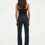 A woman viewed from behind wearing dark blue straight-leg jeans and a black strapless top against a plain white studio background.
