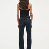 A woman viewed from behind wearing dark blue straight-leg jeans and a black strapless top against a plain white studio background.