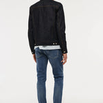 A man viewed from behind wearing a black denim jacket, a white and blue striped shirt, blue jeans, and black shoes, standing against a plain white studio background.