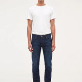A man wearing dark blue slim-fit jeans, a white t-shirt, and black shoes, standing against a plain white studio background.