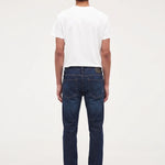 A man viewed from behind wearing a white t-shirt, dark blue jeans, and black shoes, standing against a plain white studio background.