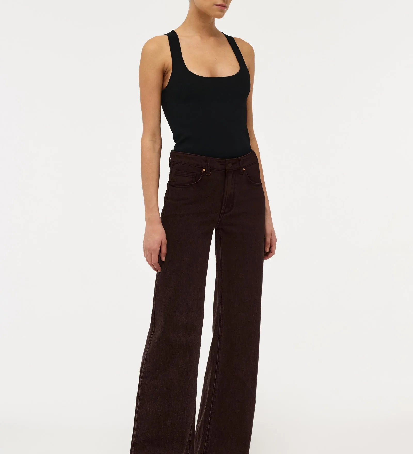 A model wearing dark brown wide-leg corduroy pants and a black tank top, standing against a plain white studio background.