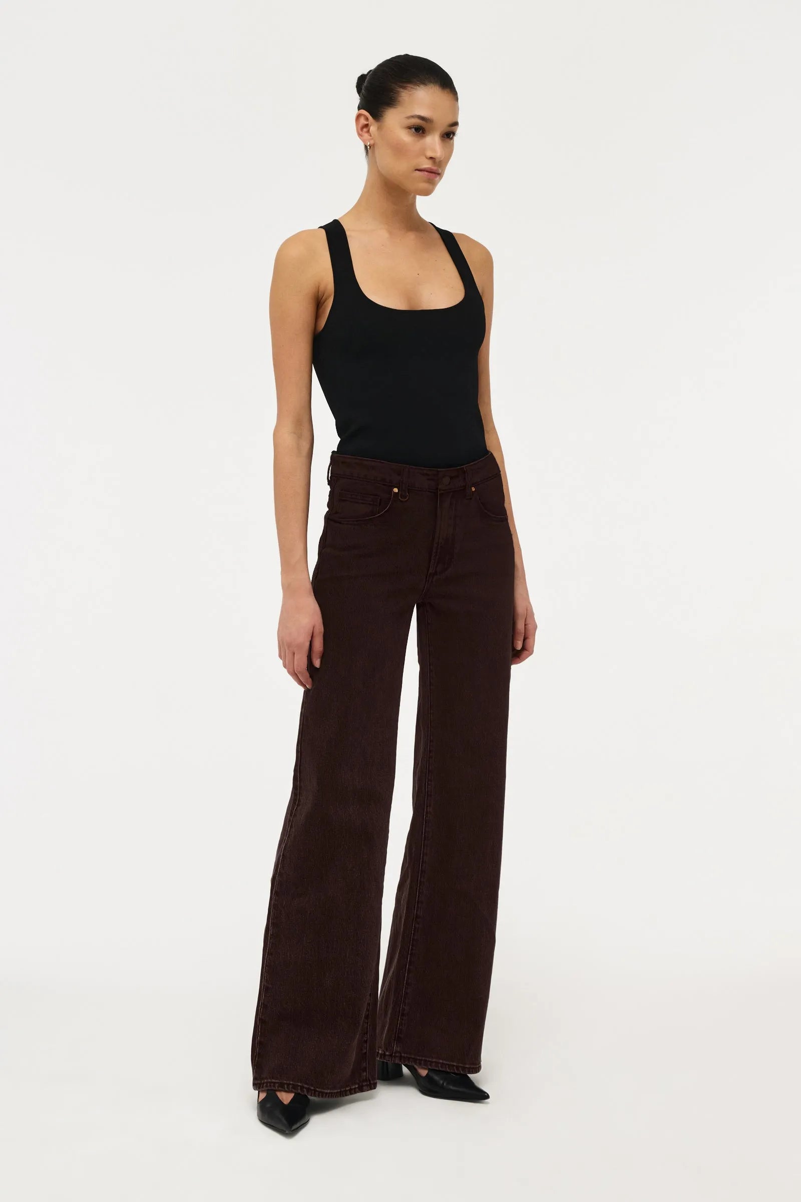 A model wearing dark brown wide-leg corduroy pants and a black tank top, standing against a plain white studio background.