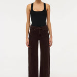 A model stands against a plain white studio background wearing a black sleeveless top and dark brown wide-leg corduroy pants.