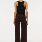 A model shown from the back wearing dark brown wide-leg corduroy pants and a black sleeveless top, standing against a plain white studio background.