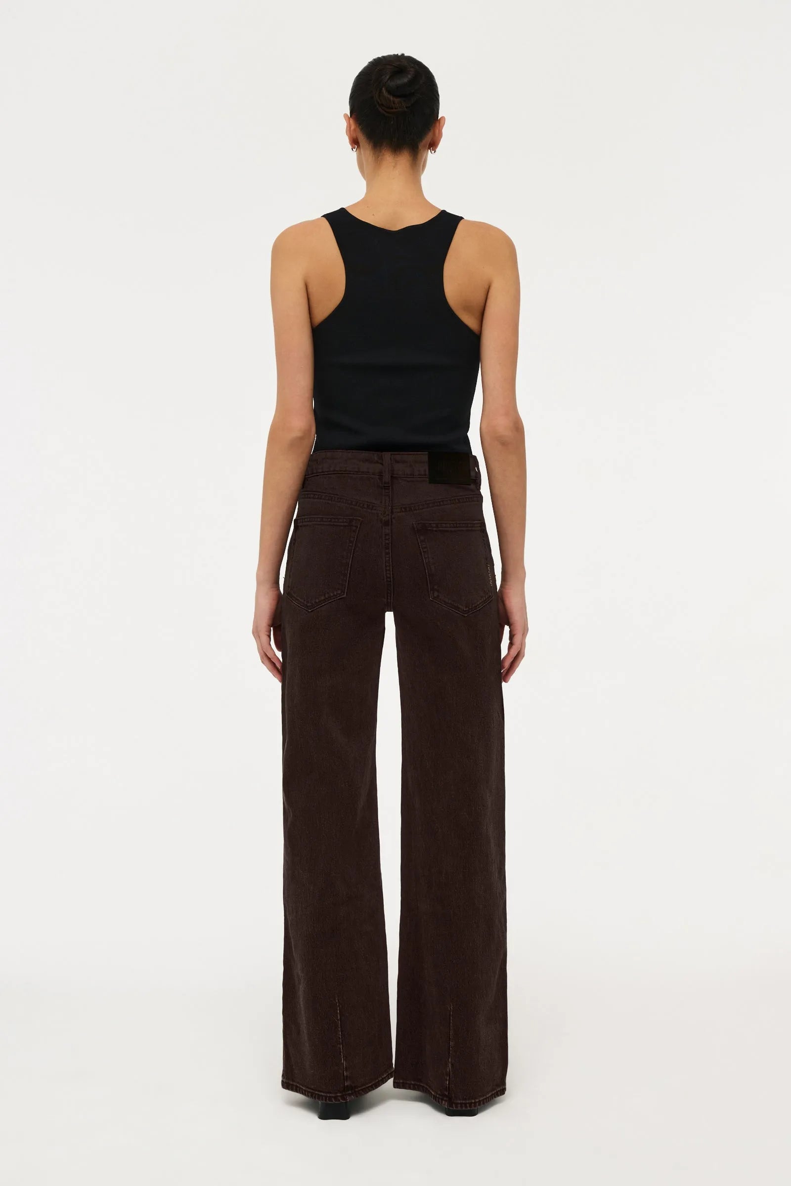 A model shown from the back wearing dark brown wide-leg corduroy pants and a black sleeveless top, standing against a plain white studio background.