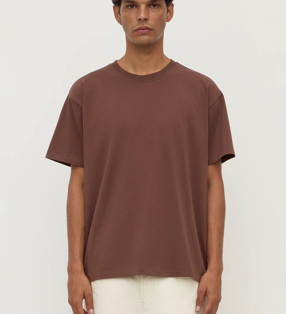 Man wearing a brown t-shirt and white pants against a white background