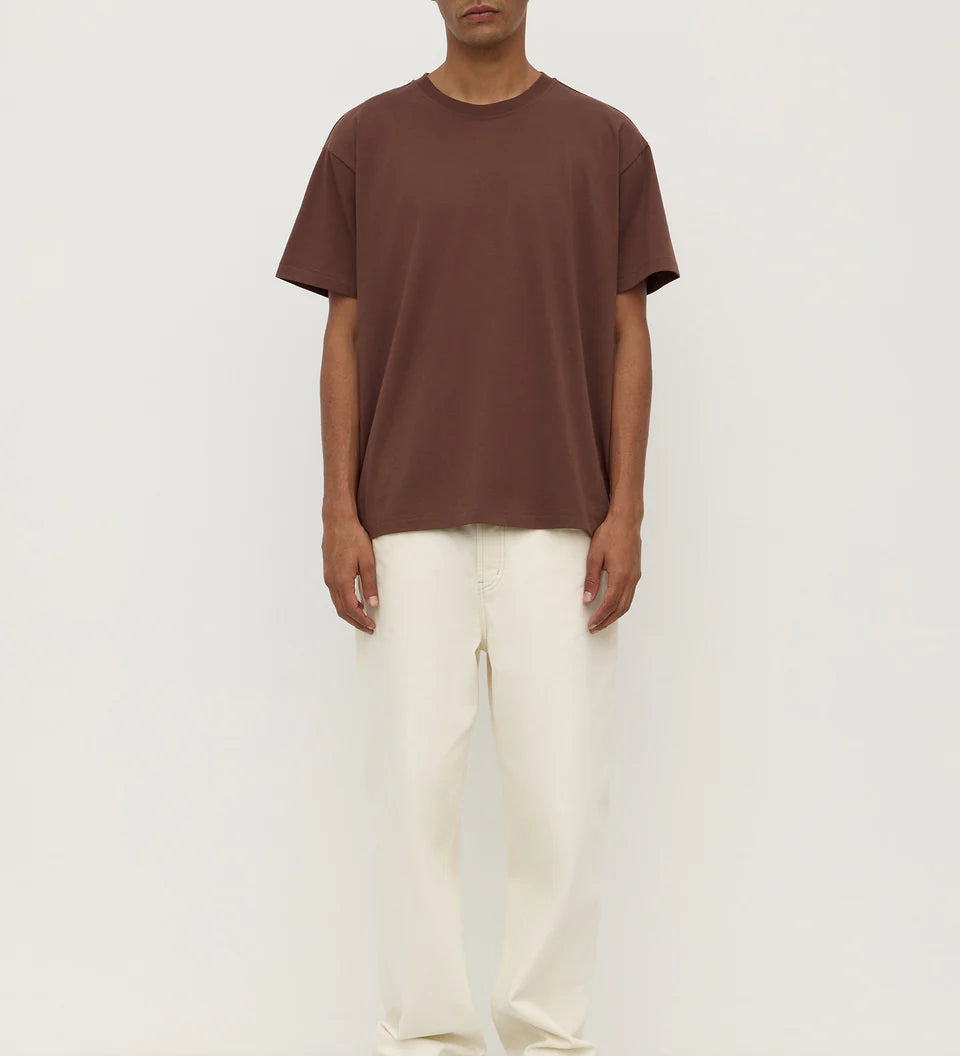 Man wearing a brown t-shirt and white pants on a white background