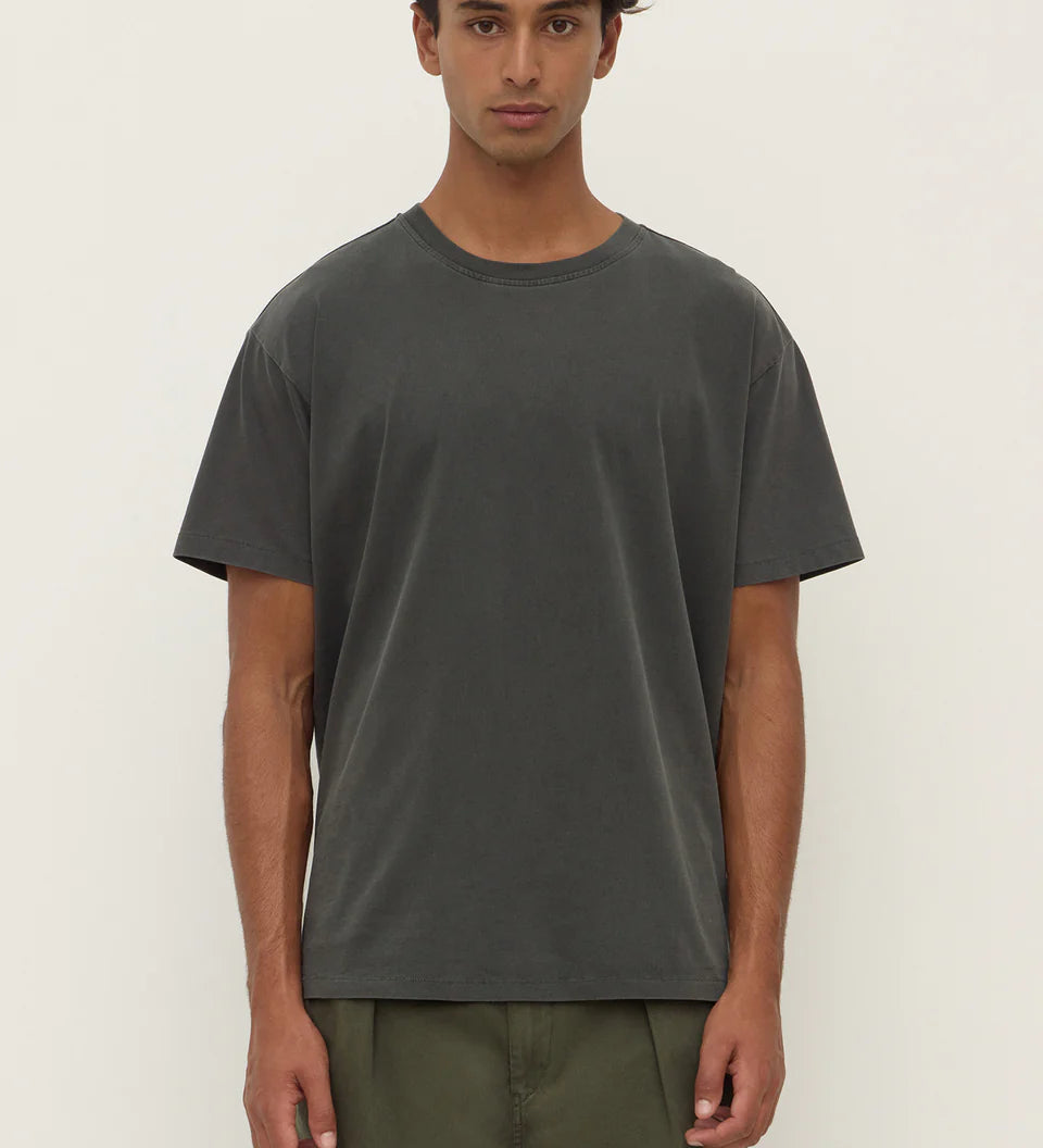 Man wearing a dark gray t-shirt and green pants on a white background
