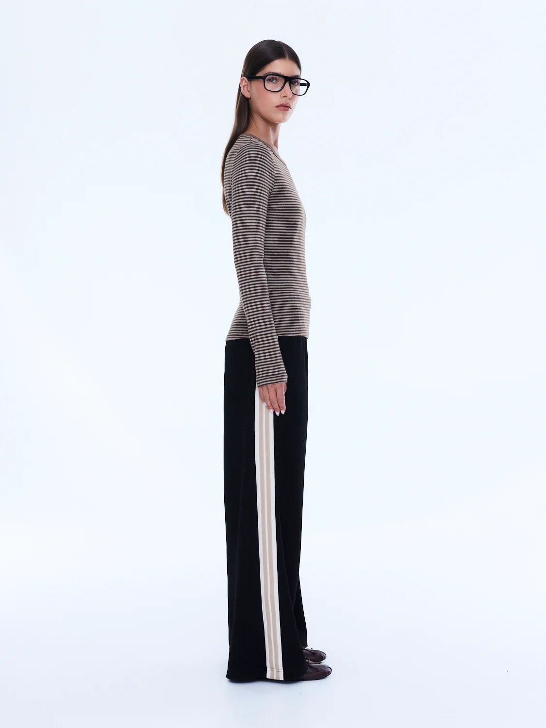 Woman wearing a striped sweater and black pants with white stripes on a white background