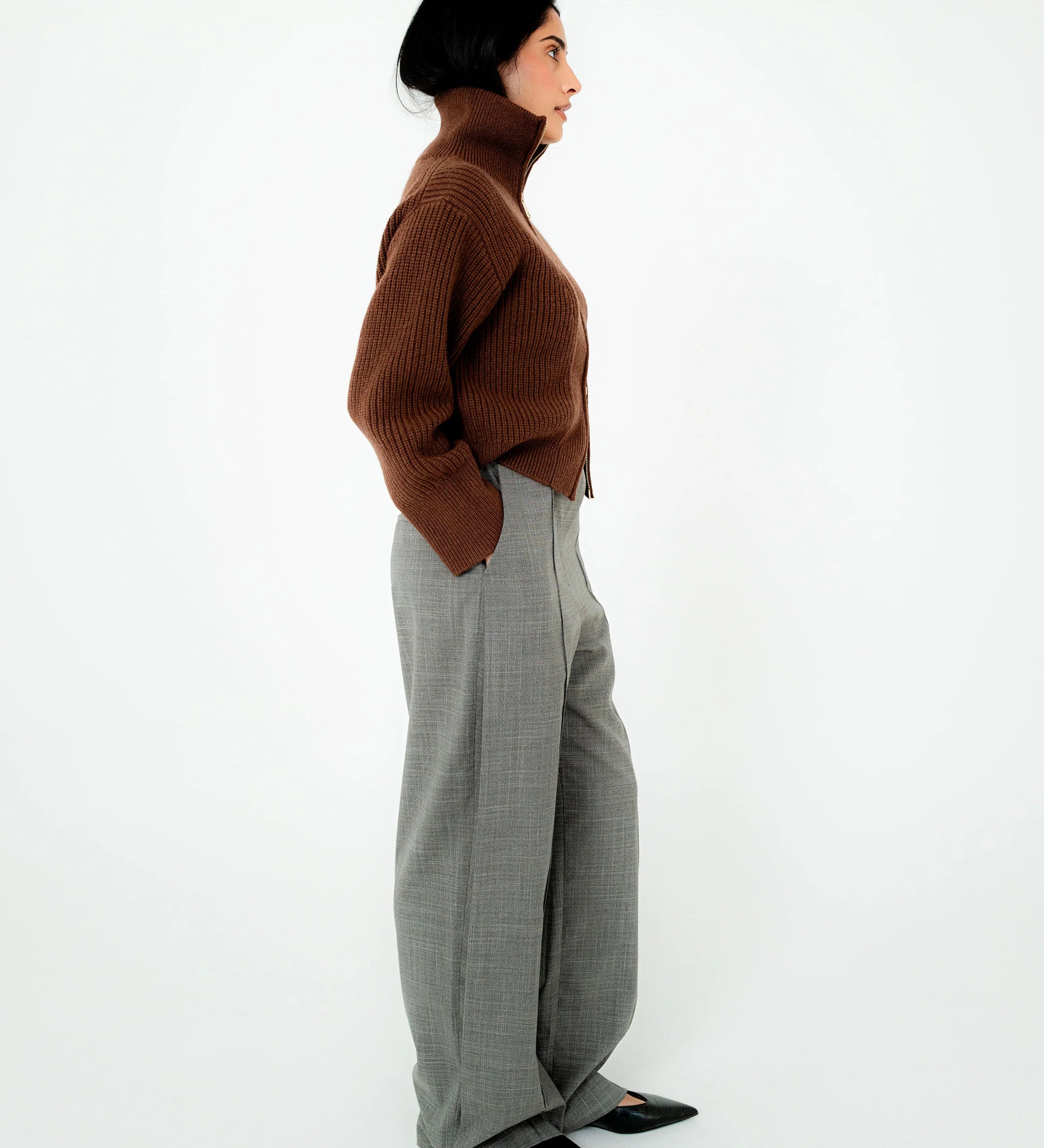 Person wearing a brown sweater and gray pants on a white background