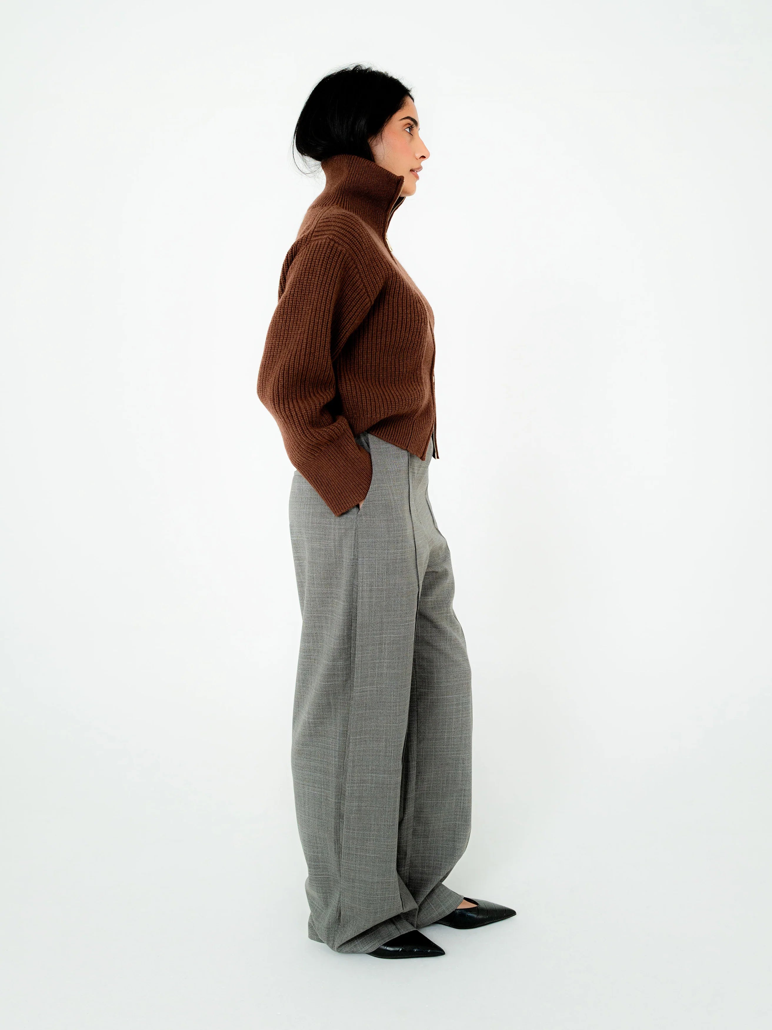 Person wearing a brown sweater and gray pants on a white background