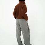 A person shown from the back wearing a brown ribbed knit mock-neck sweater and wide-leg gray trousers, standing against a plain white studio background.