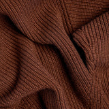 Close-up of a ribbed knit fabric in a warm rust brown color, showing the detailed texture and folds of the material.