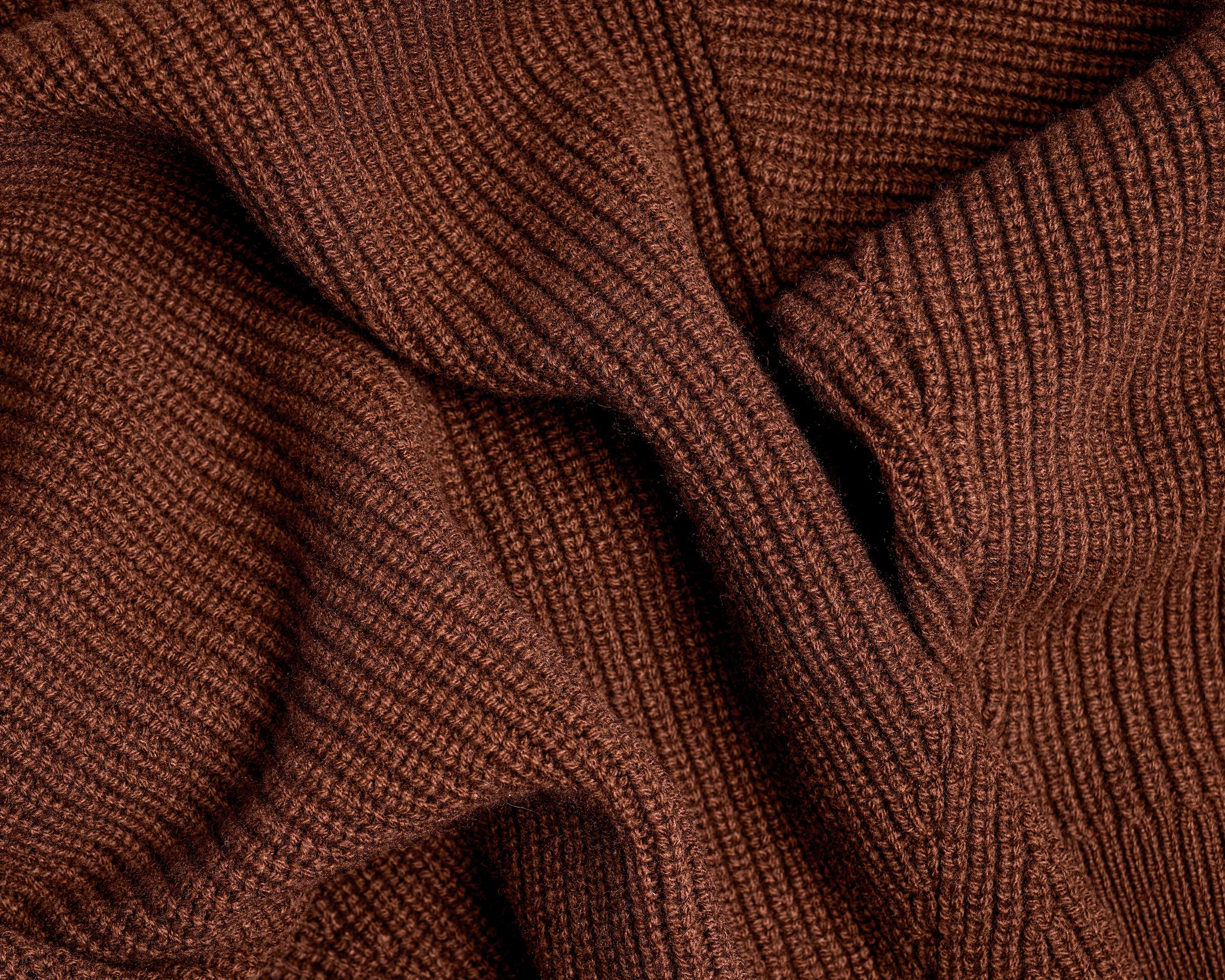 Close-up of a ribbed knit fabric in a warm rust brown color, showing the detailed texture and folds of the material.