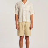 A man modeling a short-sleeve button-up shirt and beige drawstring shorts against a plain light gray studio background.