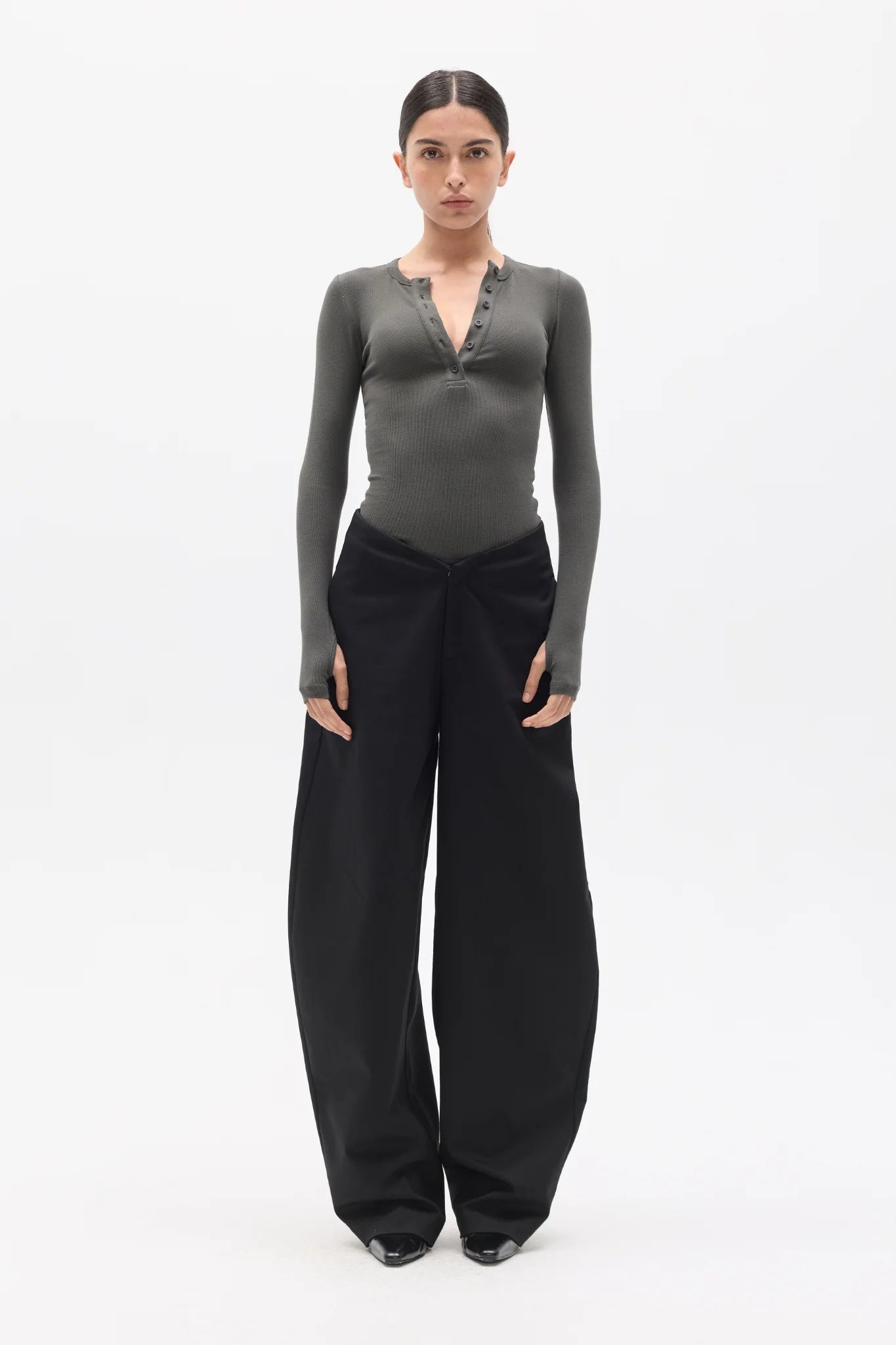 Woman wearing a gray long-sleeve top and black pants on a white background