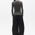 Person wearing a dark green long-sleeve top and black wide-leg pants on a white background