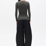 Person wearing a dark green long-sleeve top and black wide-leg pants on a white background