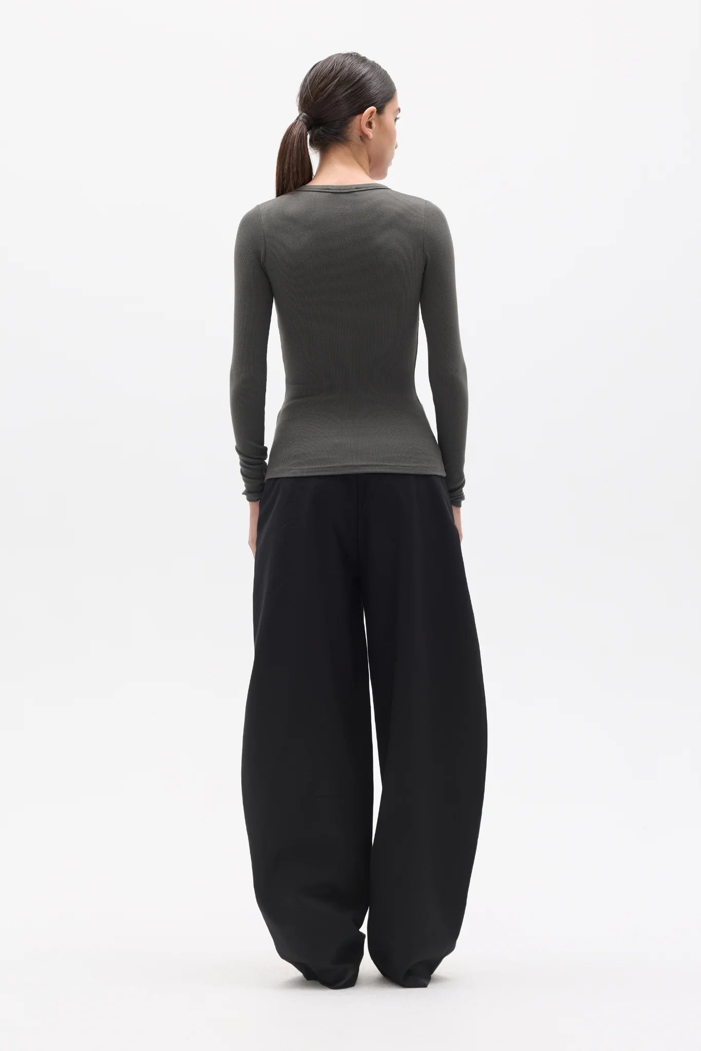 Person wearing a dark green long-sleeve top and black wide-leg pants on a white background