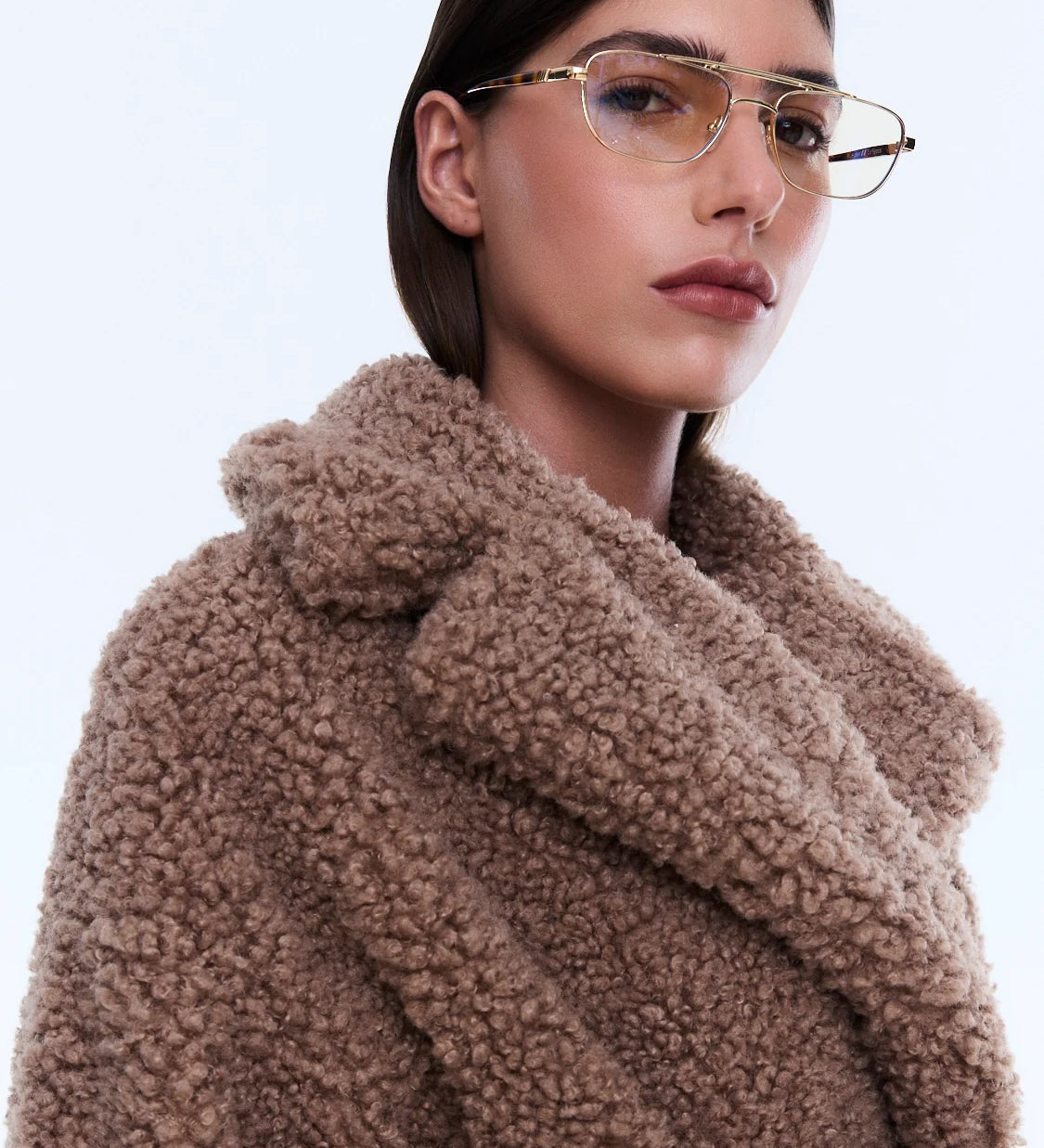 Woman wearing a brown teddy coat with a plain background
