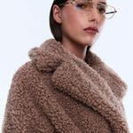Woman wearing a brown teddy coat with a plain background