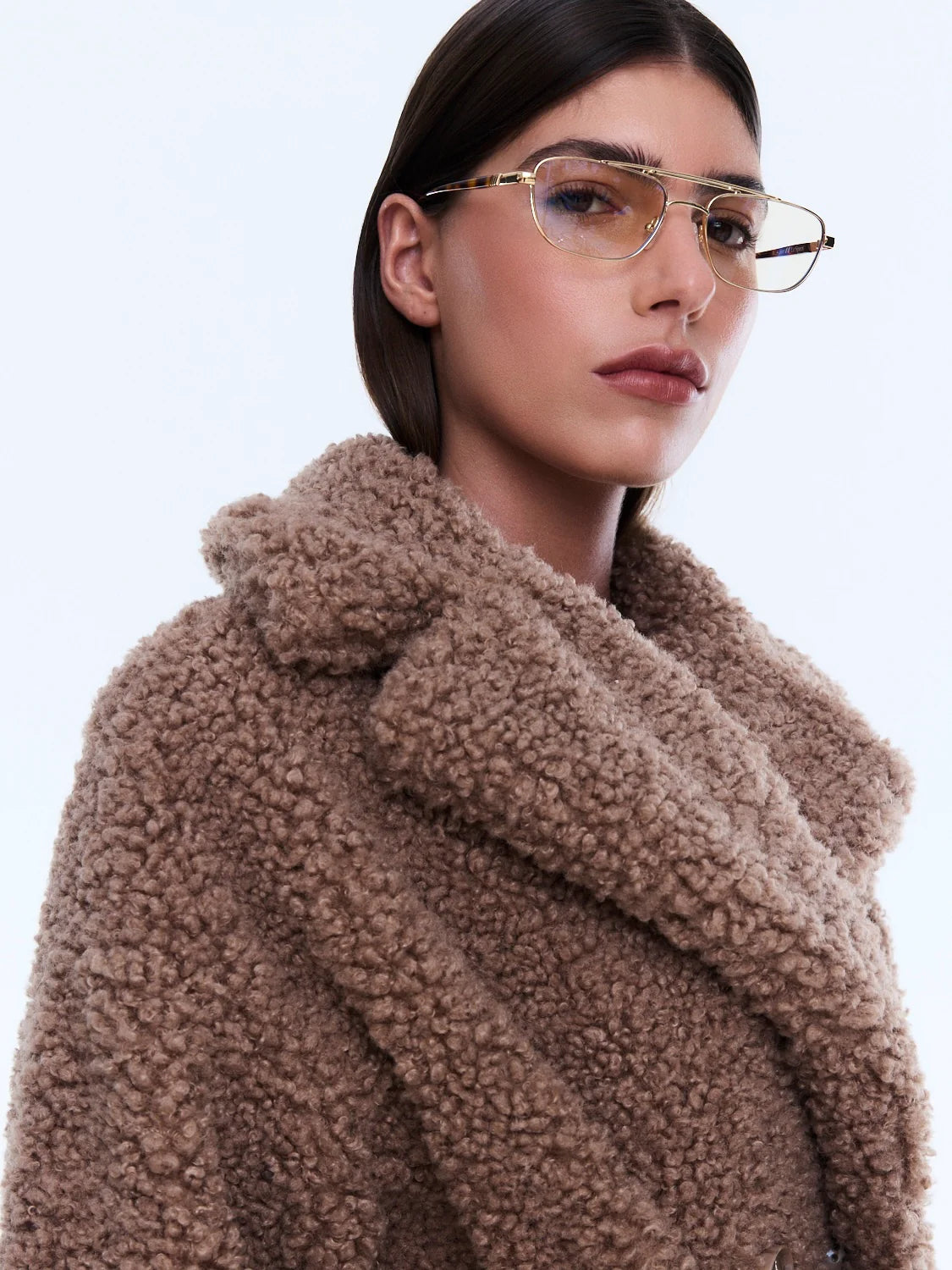 Woman wearing a brown teddy coat with a plain background
