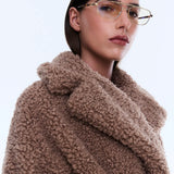 Woman wearing a brown teddy coat with a plain background
