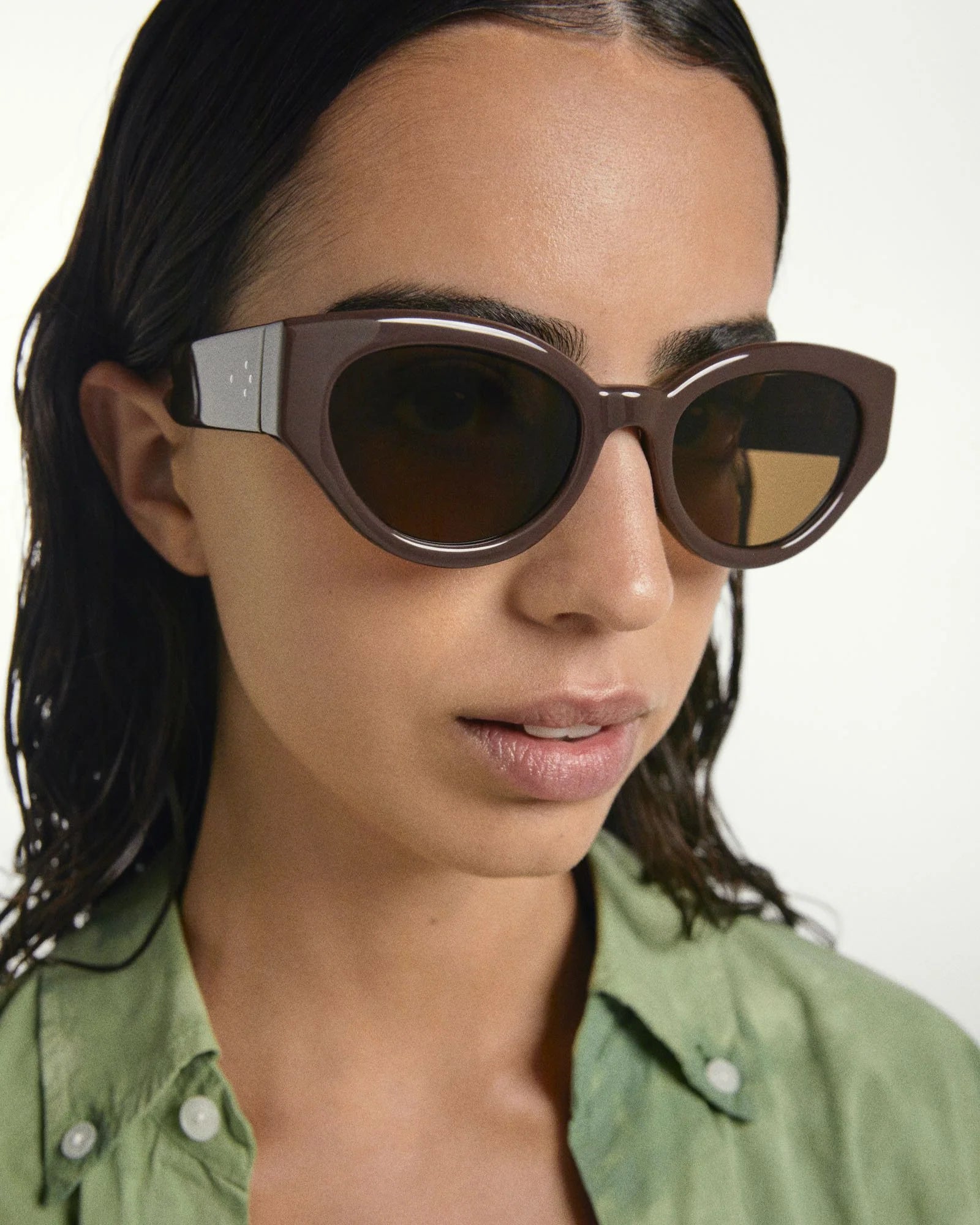 Woman wearing brown sunglasses with a green shirt on a white background