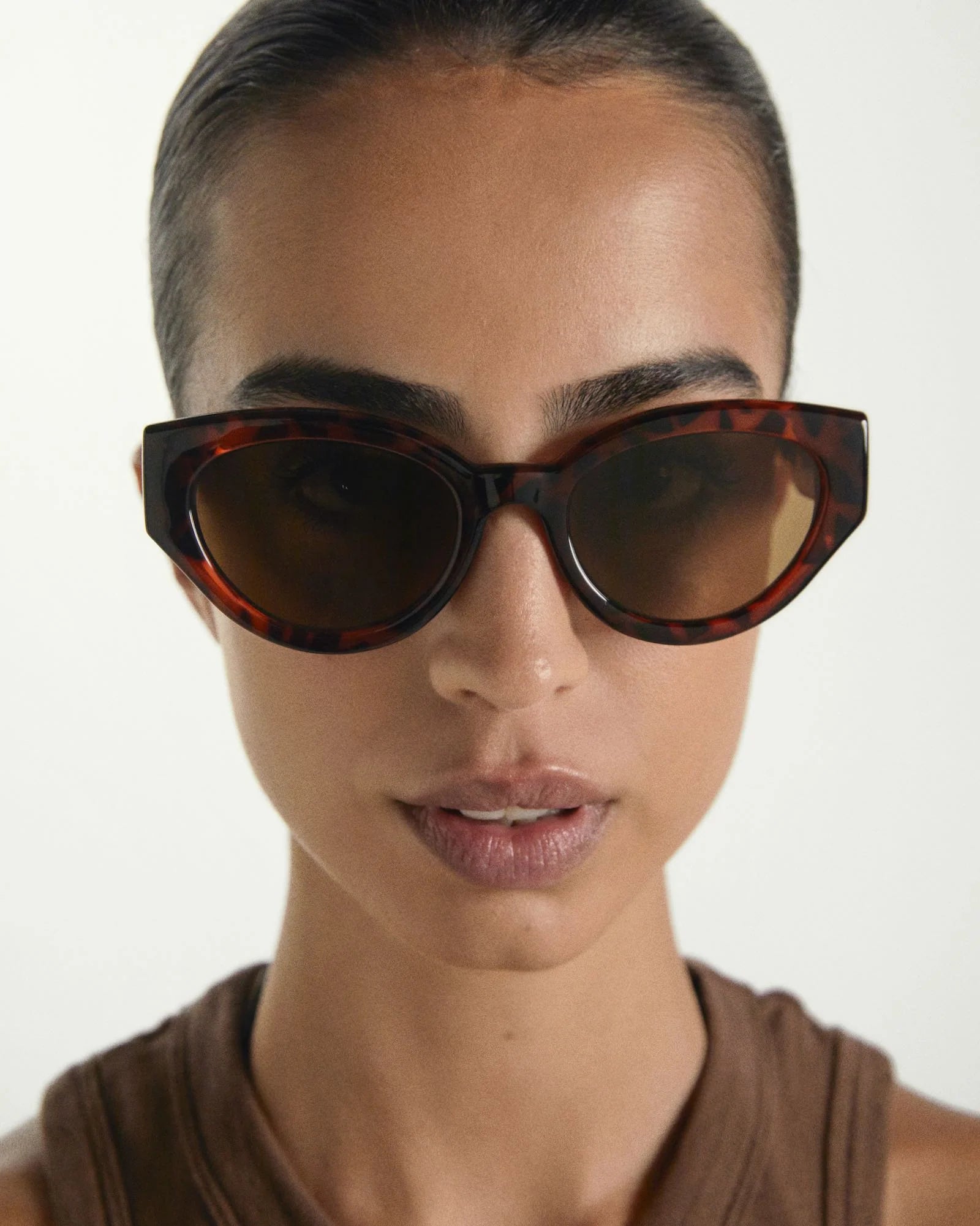 Person wearing tortoiseshell sunglasses with a neutral background