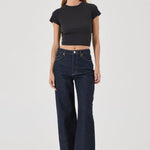 Woman wearing a black crop top and dark blue jeans on a white background