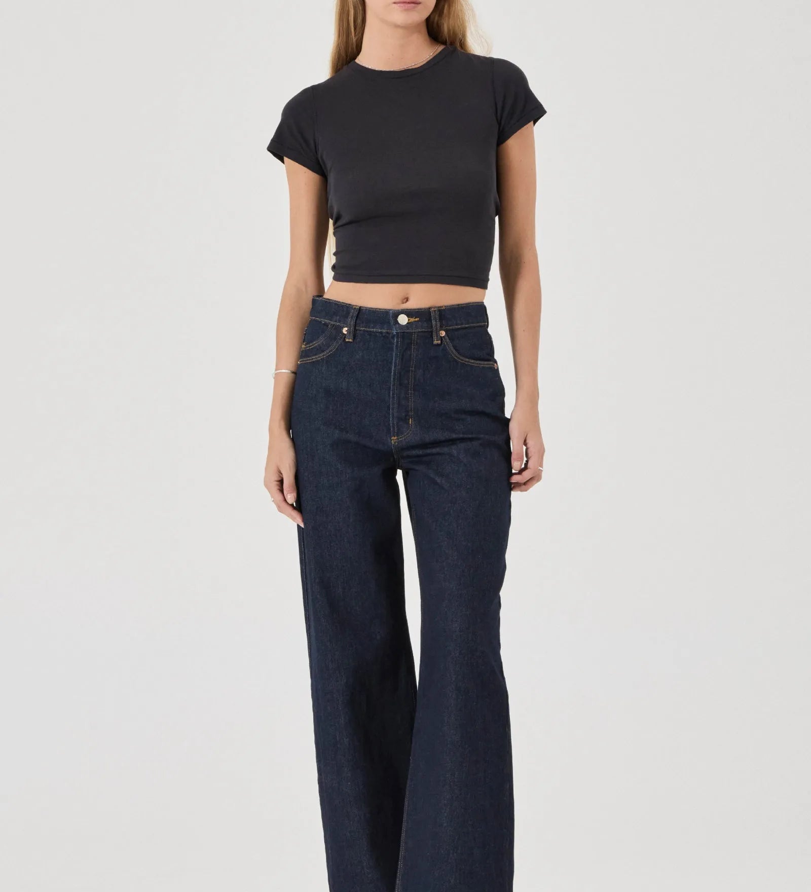 Woman wearing a black crop top and dark blue jeans on a white background