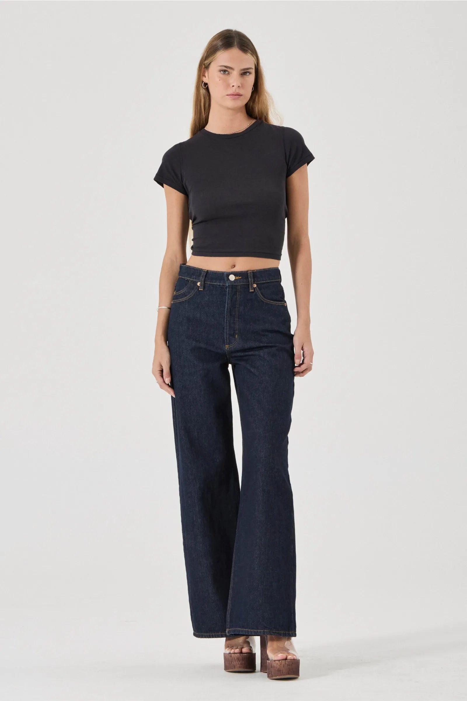 Woman wearing a black crop top and dark blue jeans on a white background