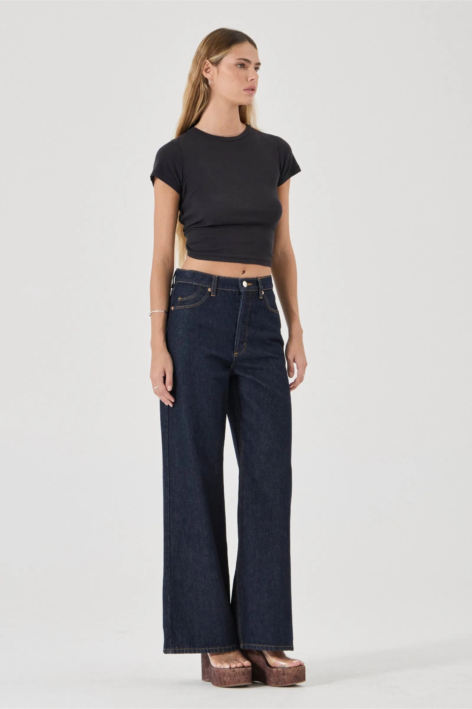 Woman wearing dark blue jeans and a black crop top on a white background