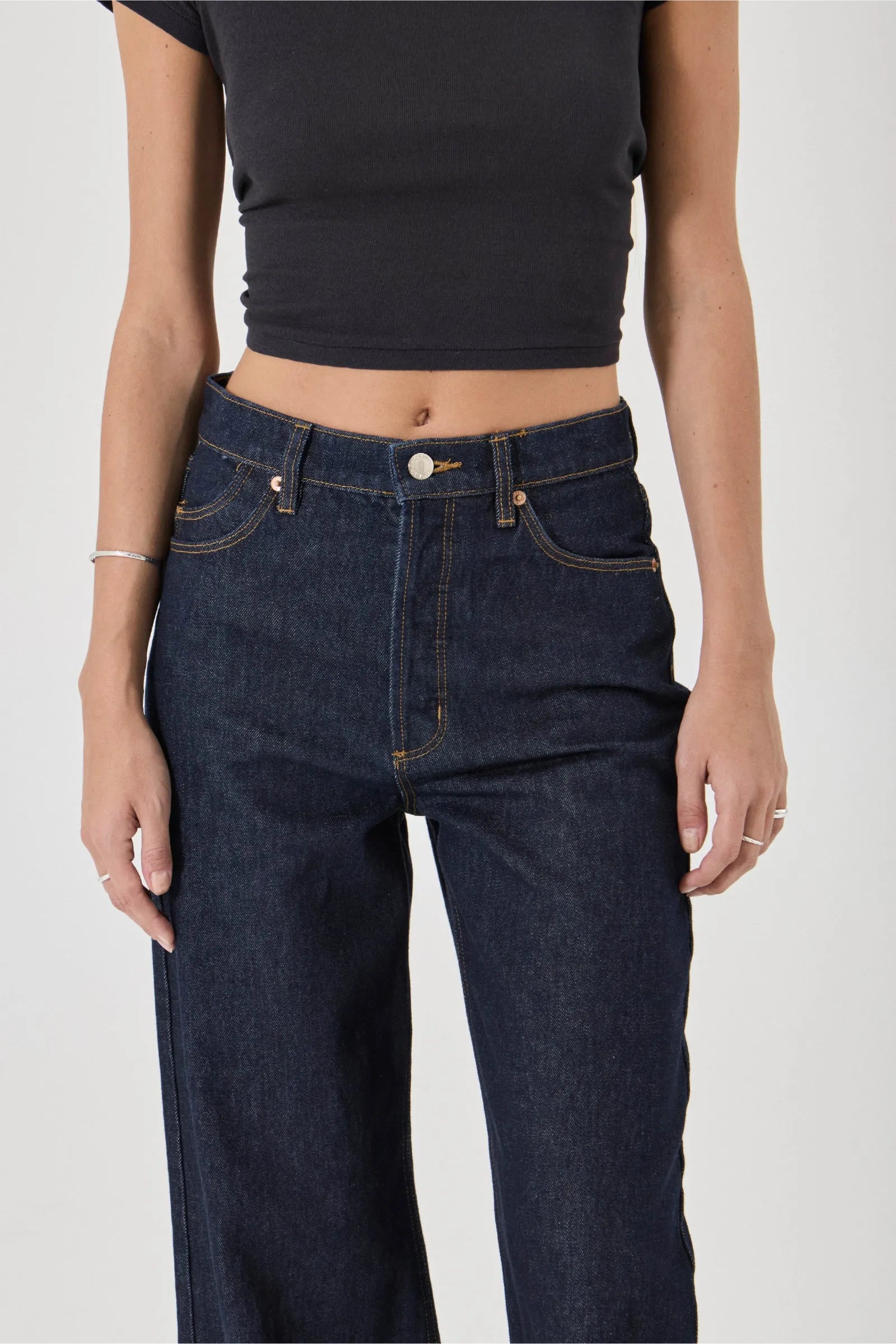 Person wearing dark blue jeans and a black crop top on a white background