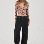 Woman wearing a patterned long-sleeve top and black pants on a white background