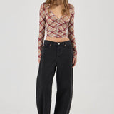 Woman wearing a patterned long-sleeve top and black pants on a white background