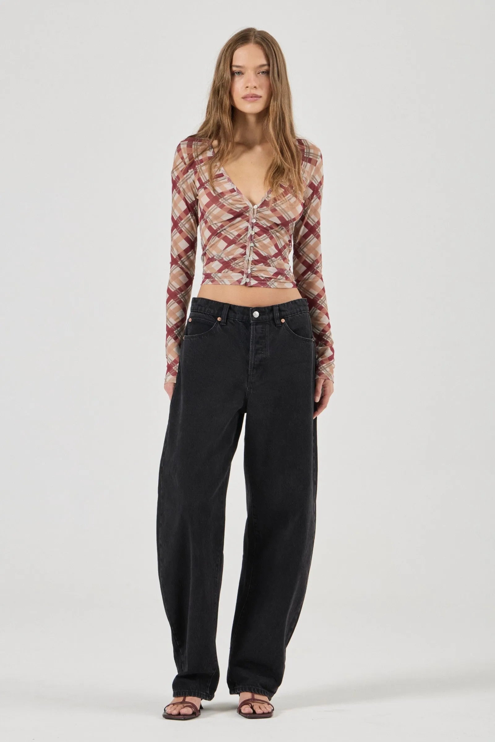 Woman wearing a patterned long-sleeve top and black pants on a white background