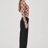 Woman wearing a patterned top and black pants on a white background