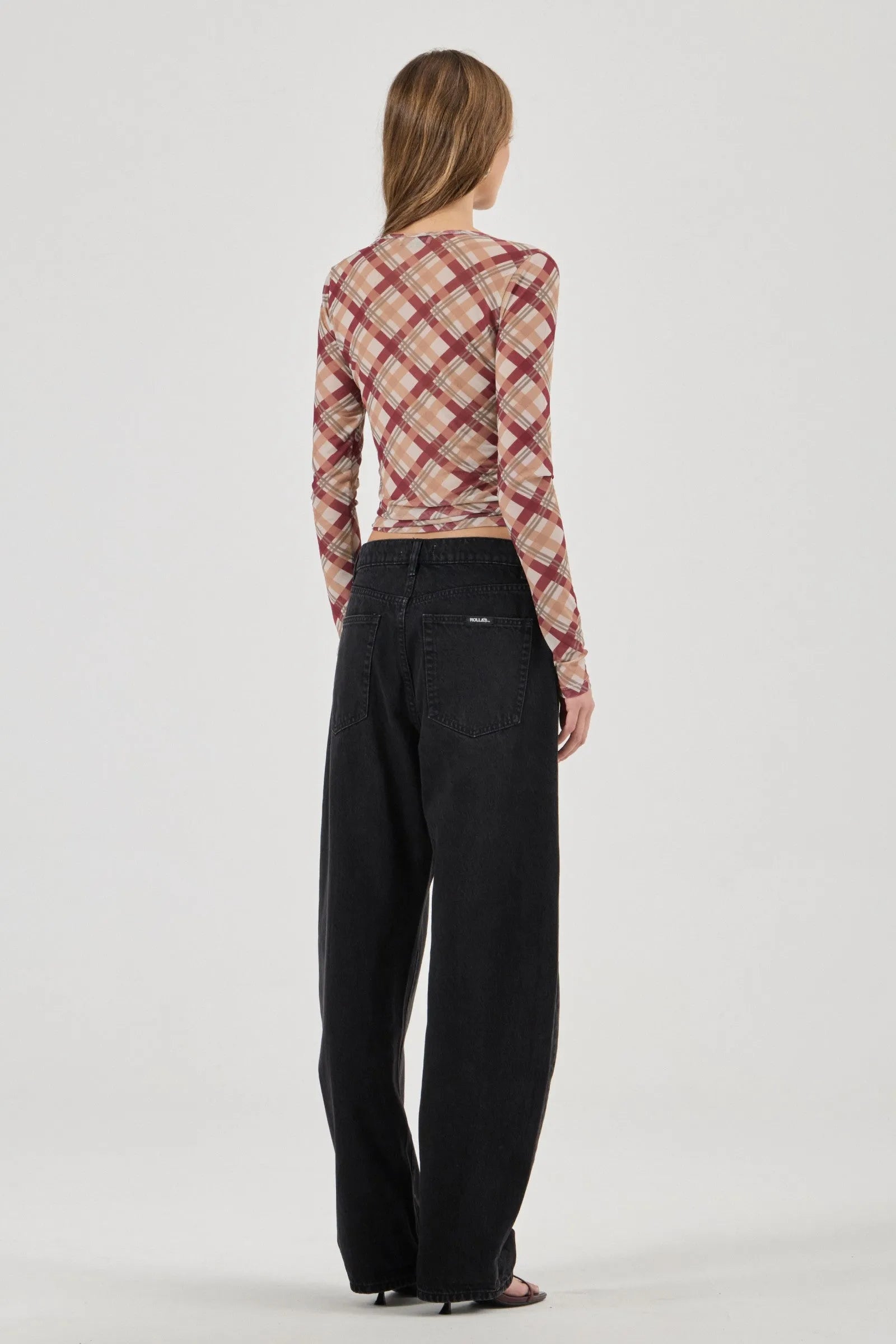Person wearing a plaid long-sleeve top and black pants on a white background