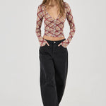 Woman wearing a patterned top and black pants on a white background