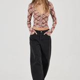 Woman wearing a patterned top and black pants on a white background
