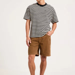 A man modeling a black and white horizontally striped short-sleeve t-shirt, brown shorts, white socks, and gray sneakers against a plain white studio background.