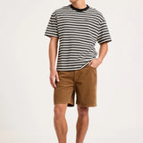 A man modeling a black and white horizontally striped short-sleeve t-shirt, brown shorts, white socks, and gray sneakers against a plain white studio background.